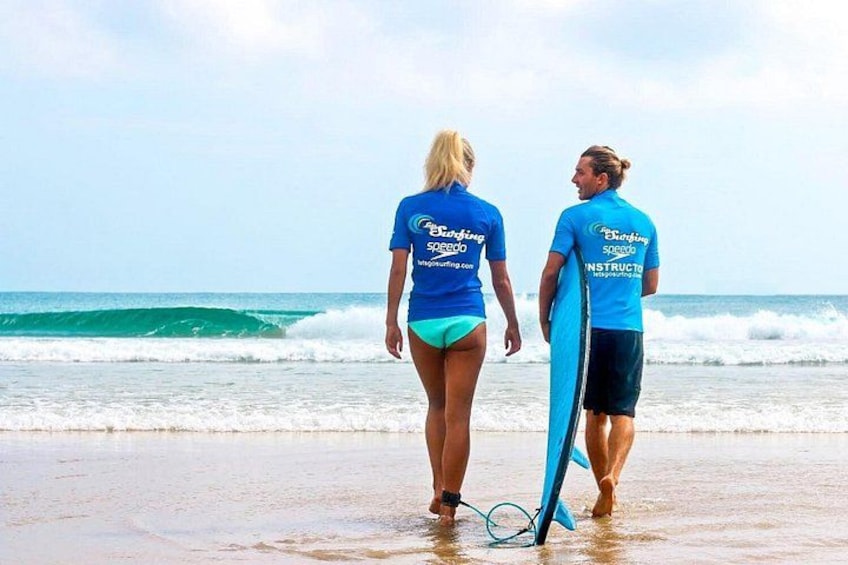 Two people walking on a beach with surfboards, ocean waves, and a clear sky. 1