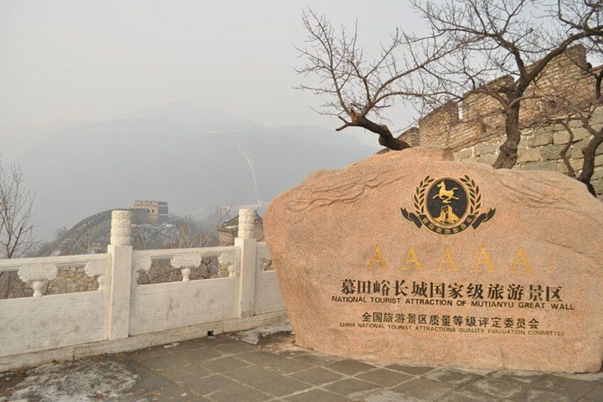 Una gran piedra con inscripciones y un logotipo, una cerca blanca y un muro de piedra en una zona montañosa. 3