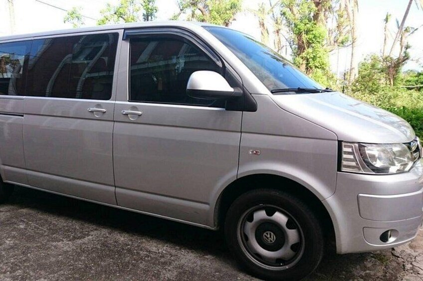 A silver van parked on a concrete surface with a Volkswagen logo on the front wheel. 1