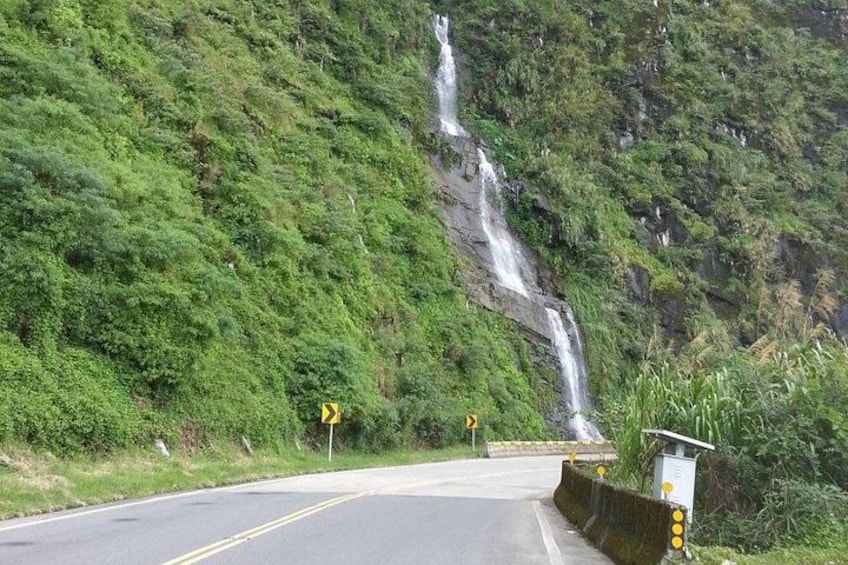 A road curving around a waterfall, surrounded by lush greenery. 4