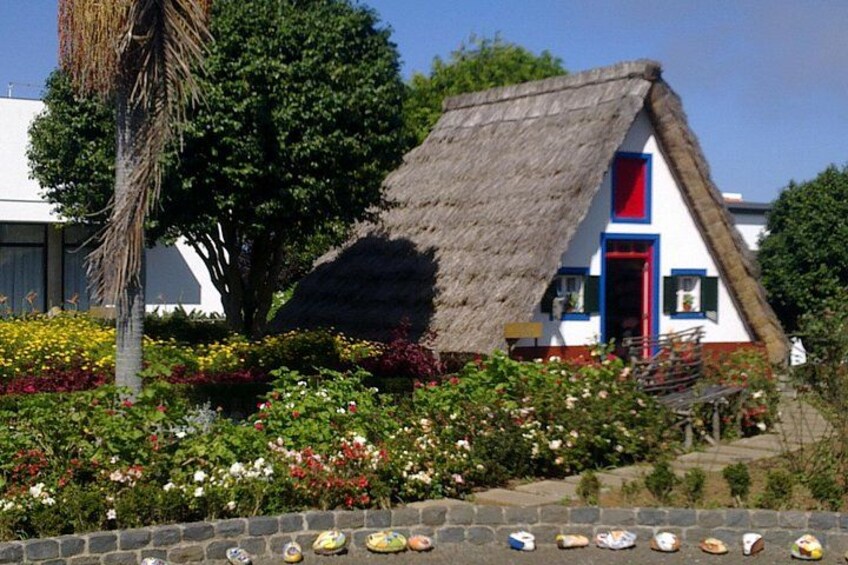 A thatched-roof house with a red door, surrounded by colorful flowers and a stone wall with baked goods. 5