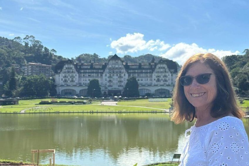 A woman in front of a historic building with a lake and trees in the background. 1