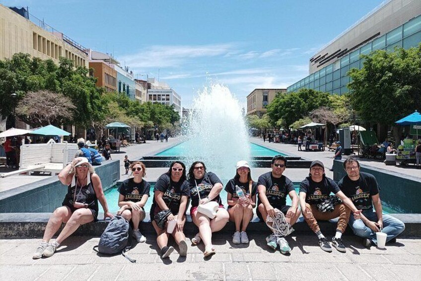 A group of people sitting by a fountain in an urban setting with buildings and trees in the background. 4