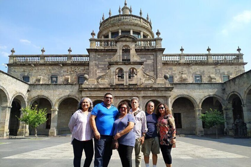 A group of people standing in front of a historic building with arches and a dome. 1