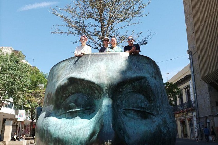 A large bronze statue of a man's face with people sitting on top. 5