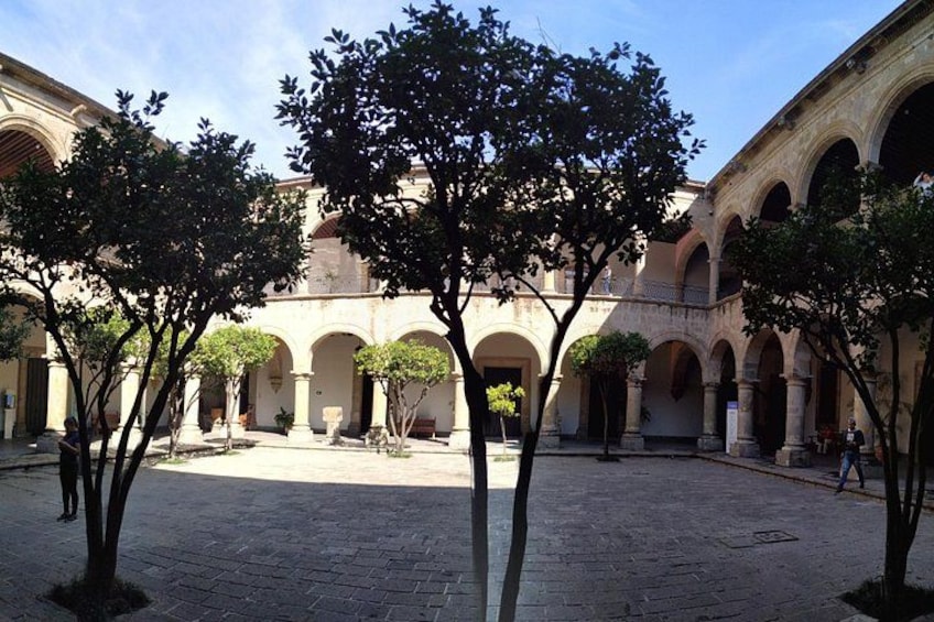 A courtyard with arches, trees, and a paved ground. 5