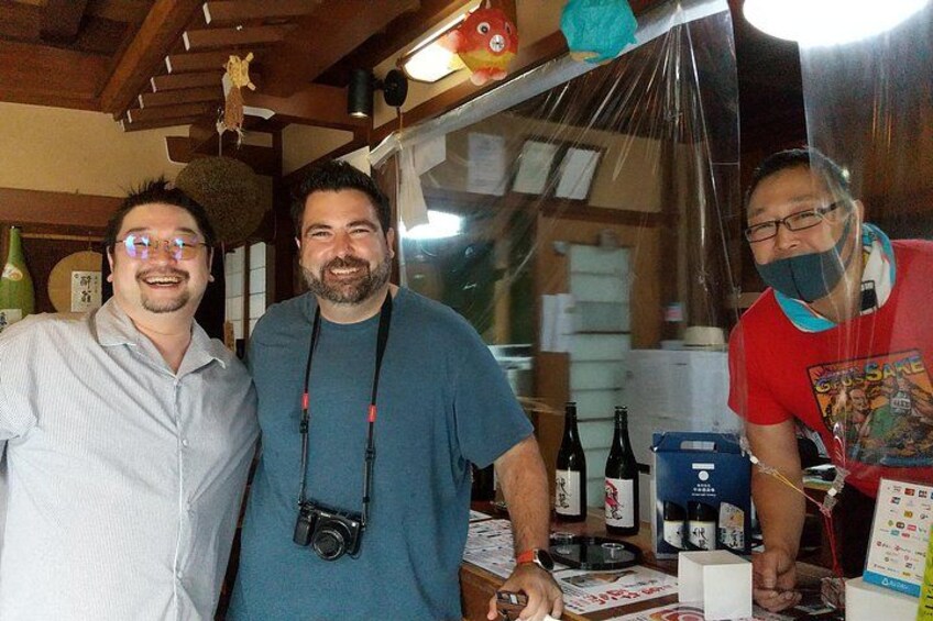 Tre persone in piedi al bancone, con bottiglie e scatole, forse in un bar o ristorante. 3