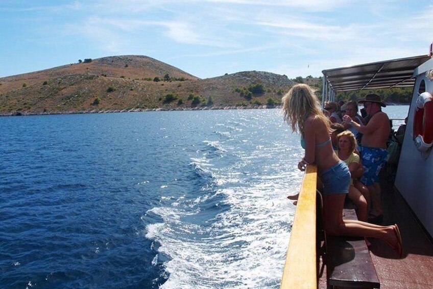 Ein Boot auf dem Wasser mit Personen an Bord, eine hügelige Landschaft im Hintergrund und ein klarer Himmel. 4