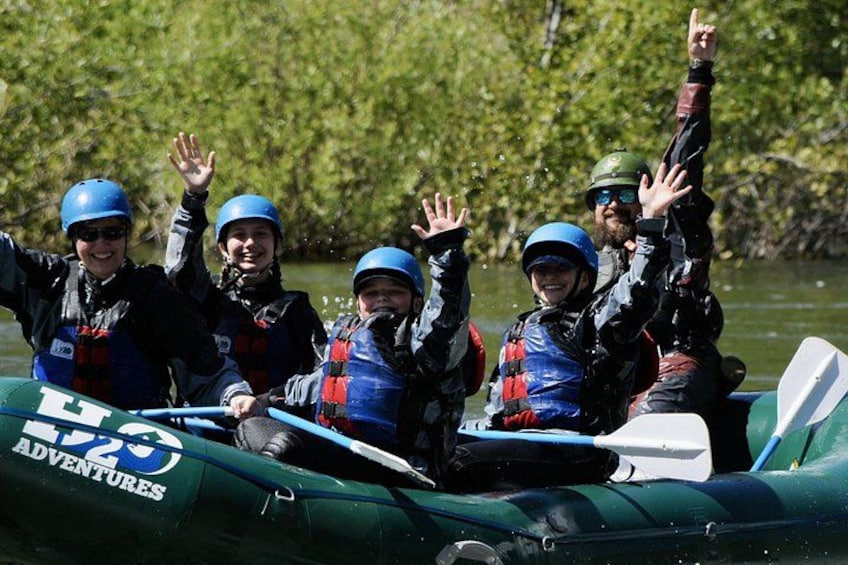 A group of people in a green inflatable raft on a river, wearing helmets and life jackets. 2