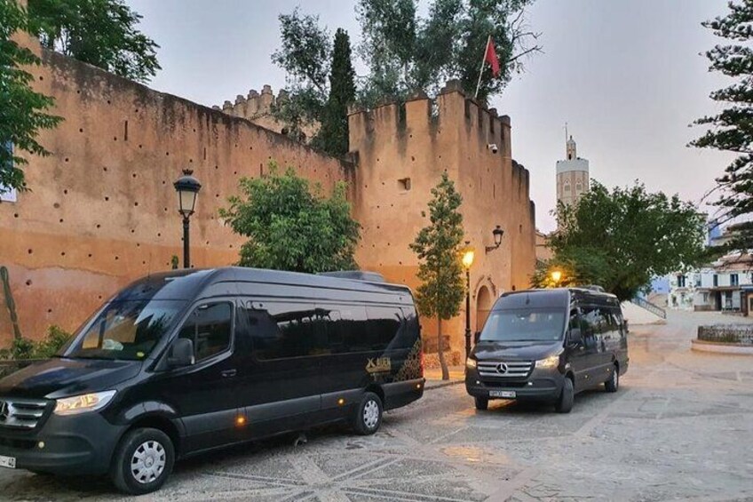 A black van parked on a cobblestone street with a historic wall and a tower in the background. 4