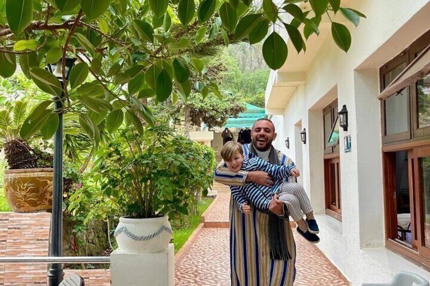 A man carrying a child on a balcony with potted plants and a building in the background. 5