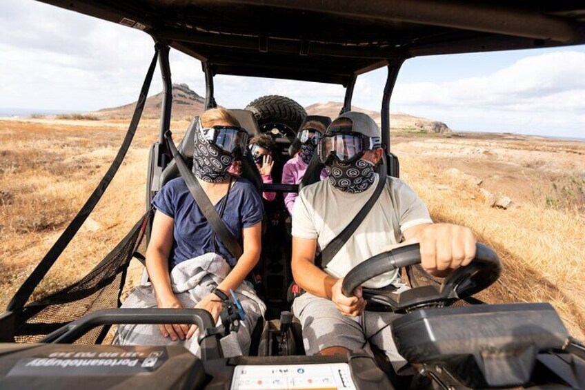 A vehicle on a dirt road with three people wearing helmets and a bandana. 4