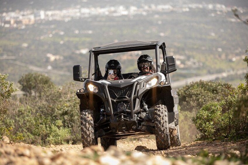 A four-wheeled vehicle on a dirt path with a hilly landscape in the background. 1