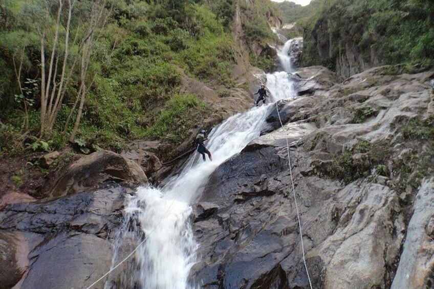 A person rappelling down a waterfall in a rocky, forested area. 3