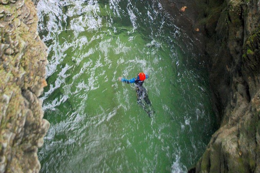 Una persona con traje de neopreno azul y casco rojo nadando en aguas verdes rodeada de acantilados rocosos. 5