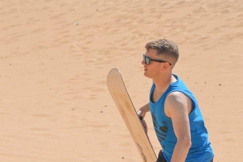Una persona sosteniendo una tabla de snowboard, con una camiseta azul sin mangas, de pie sobre una superficie arenosa. 5