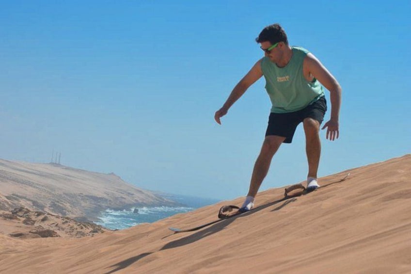 Una persona equilibrándose sobre una duna de arena, con un cielo despejado y el océano al fondo. 4