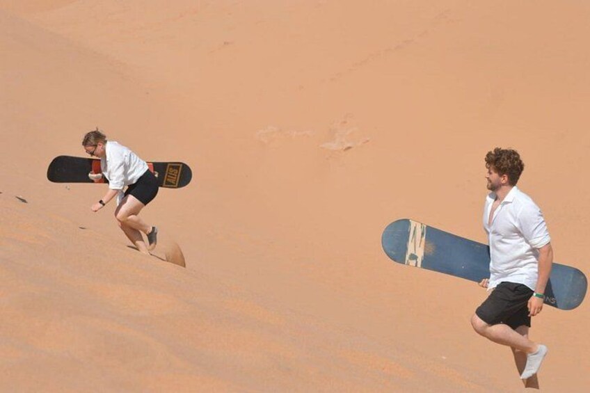 Dos personas corriendo sobre terreno arenoso con tablas de snowboard. 3