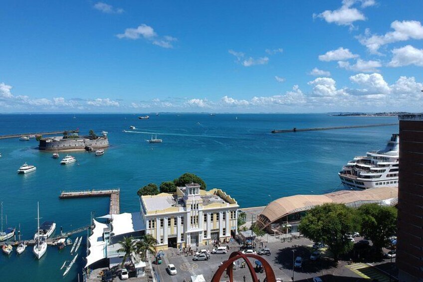 A coastal cityscape with a historic fort, a cruise ship docked, and a marina with boats. 4