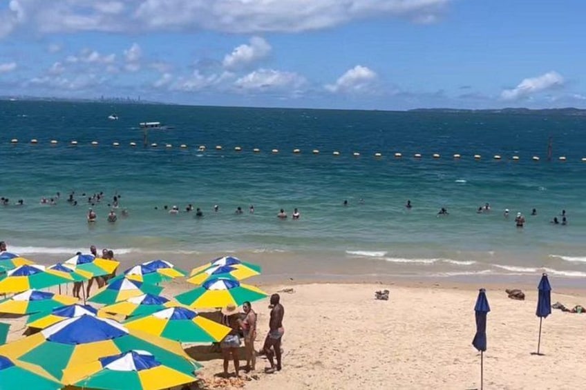 A beach with people swimming and sunbathing, umbrellas, and a clear sky. 3
