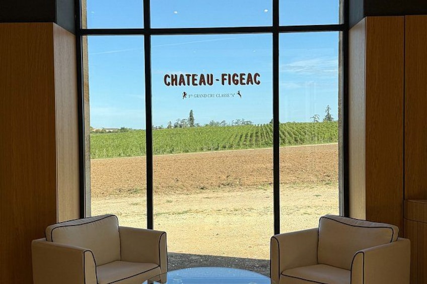 A view of Chateau-Figeac vineyard through large windows, with two beige chairs in the foreground. 3
