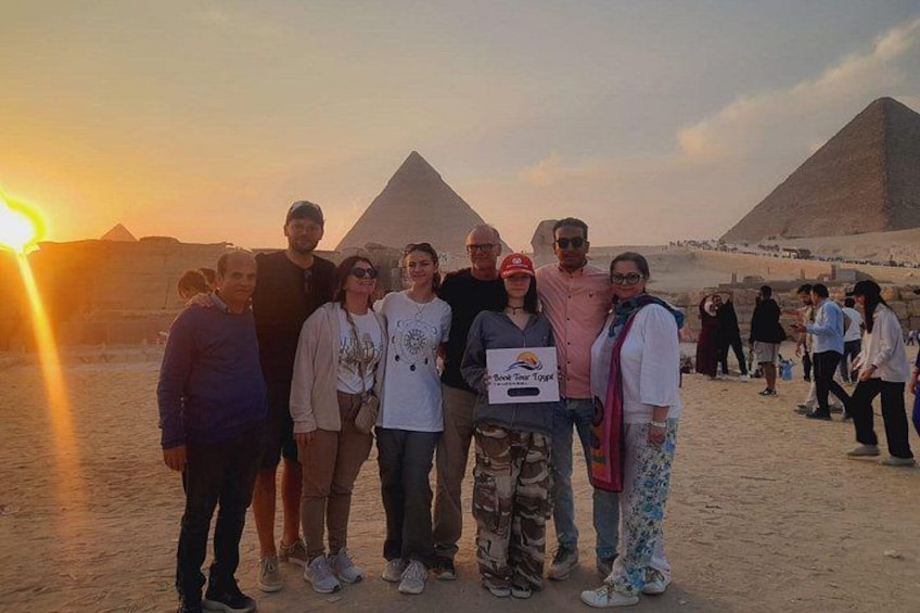A group of people standing in front of the pyramids at sunset. 2