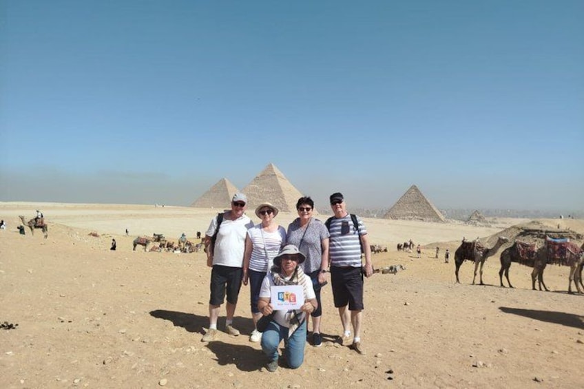 A group of people in a desert with pyramids in the background. 2