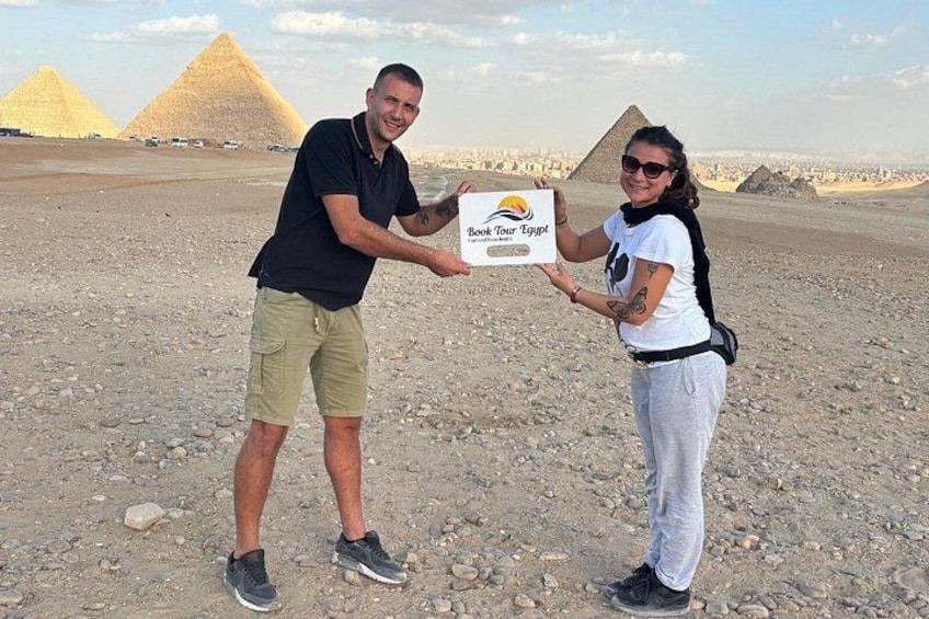 Two people holding a sign with 'Book 'Tour Egypt' written on it, standing in front of pyramids. 4