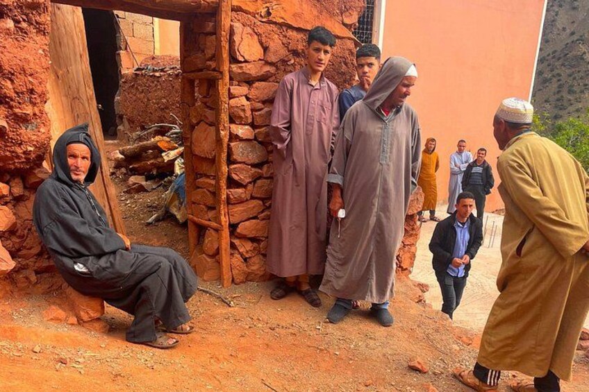A group of people in traditional attire standing and sitting outdoors near a stone structure. 3