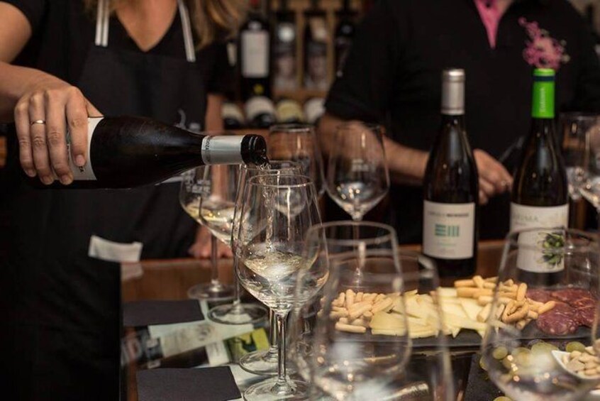 Une personne verse du vin dans un verre. Plusieurs bouteilles de vin et des verres sont posés sur la table. 2
