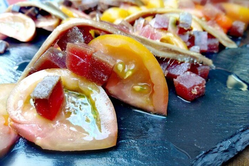 Une vue rapprochée d’une assiette sombre sur laquelle on voit des tomates et des oignons coupés en tranches, ainsi que d’autres légumes. 3