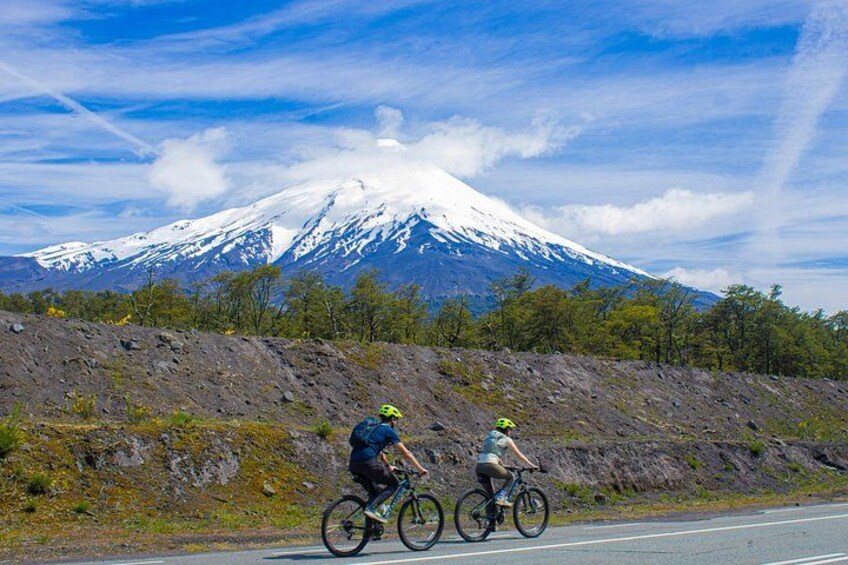 Two cyclists on a road with a snow-capped mountain in the background. 1
