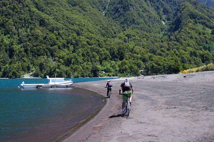 A beach with cyclists, a boat, and a forested hill in the background. 2