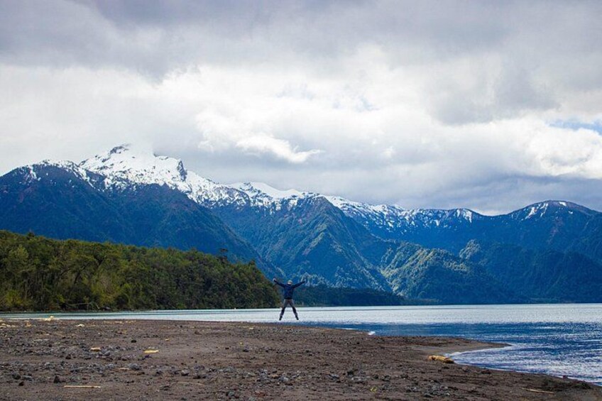 A person standing on a rocky shore with mountains in the background. 4