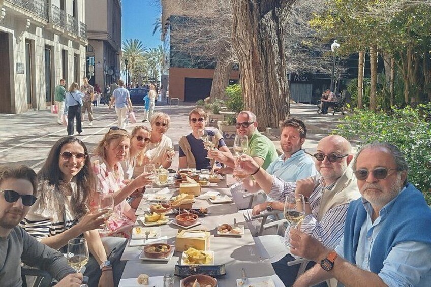 Un grupo de personas sentadas alrededor de una mesa al aire libre, disfrutando de una comida con diversos platos y bebidas. 2