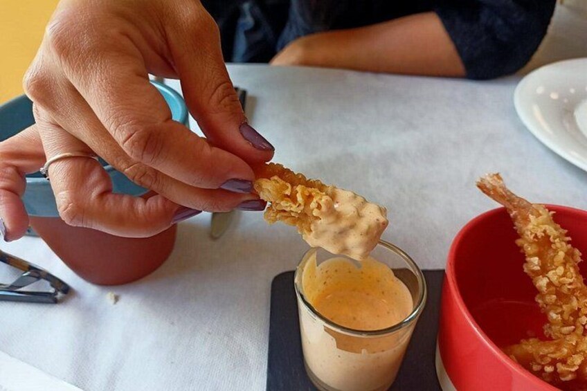 Una mano sumergiendo un alimento frito en un vaso de salsa. 5