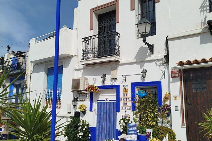 Un edificio blanco con puertas y ventanas azules, un balcón con barandillas negras y una farola. 4