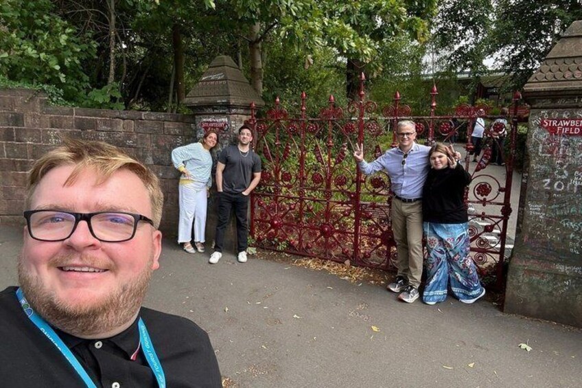 A group of people standing by a red iron gate with a sign that reads 'Strawberry Field.' 5