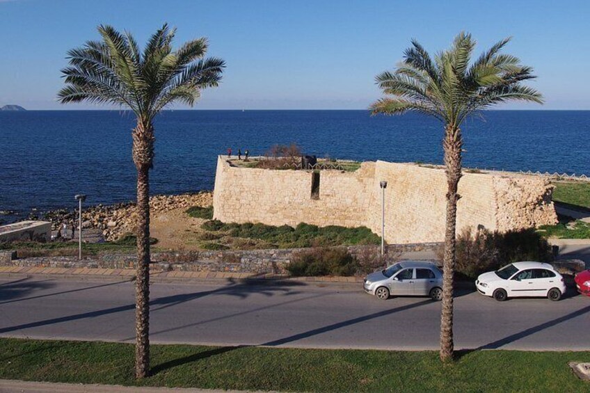 A coastal road with palm trees, a stone wall, and a view of the sea. 4