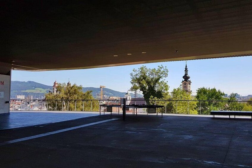 Una estructura al aire libre con bancos, barandilla y vista a una torre de reloj distante. 1