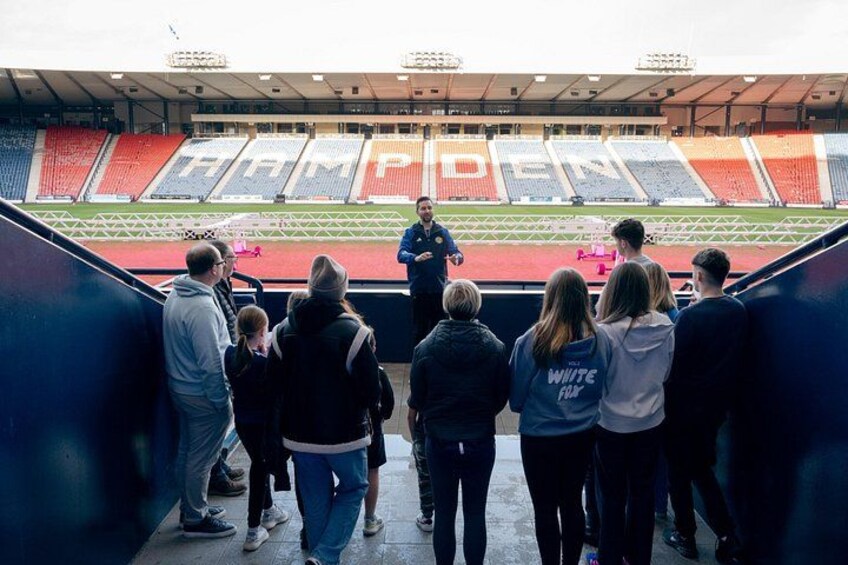 A tour guide shows visitors the pitch and stadium bowl from the trophy presentation area 2