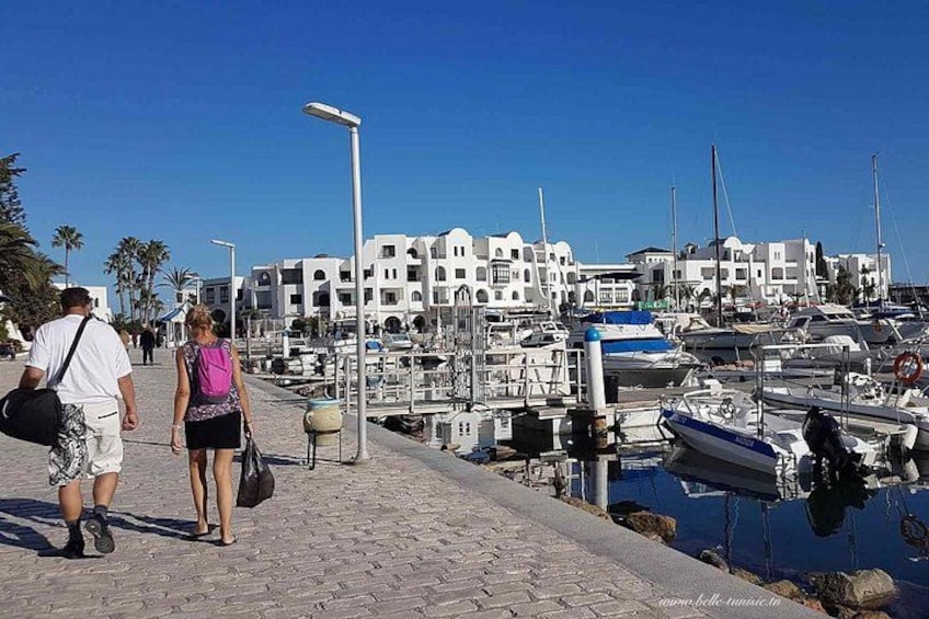 Un marina con barche ormeggiate, una passeggiata pedonale e edifici bianchi sullo sfondo. 1