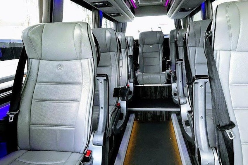 Interior de autobús con asientos de cuero gris, compartimentos de almacenamiento superiores y un pasillo central. 5