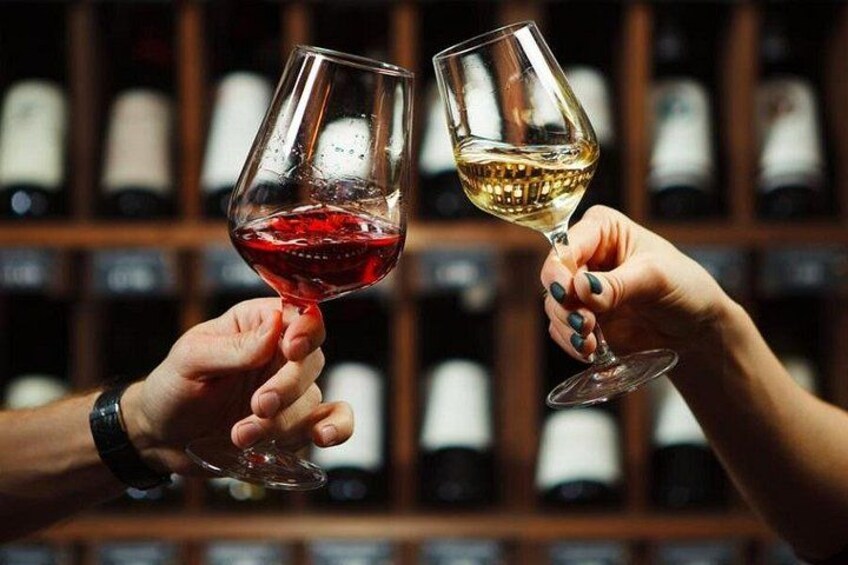 Two hands holding wine glasses, one with red wine and the other with white wine, in front of a blurred background of wine bottles. 1
