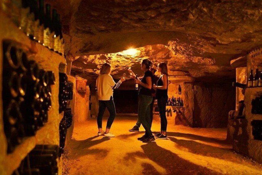 A cave with wine bottles on shelves, a person holding a bottle, and another person standing nearby. 5