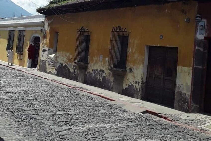 A cobblestone street with a yellow building, a window with a metal grill, and a door. 3