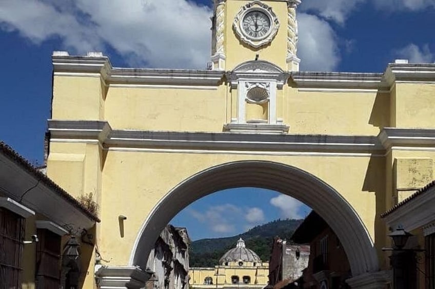 A yellow archway with a clock tower, a mountain in the background, and a building with a dome. 5