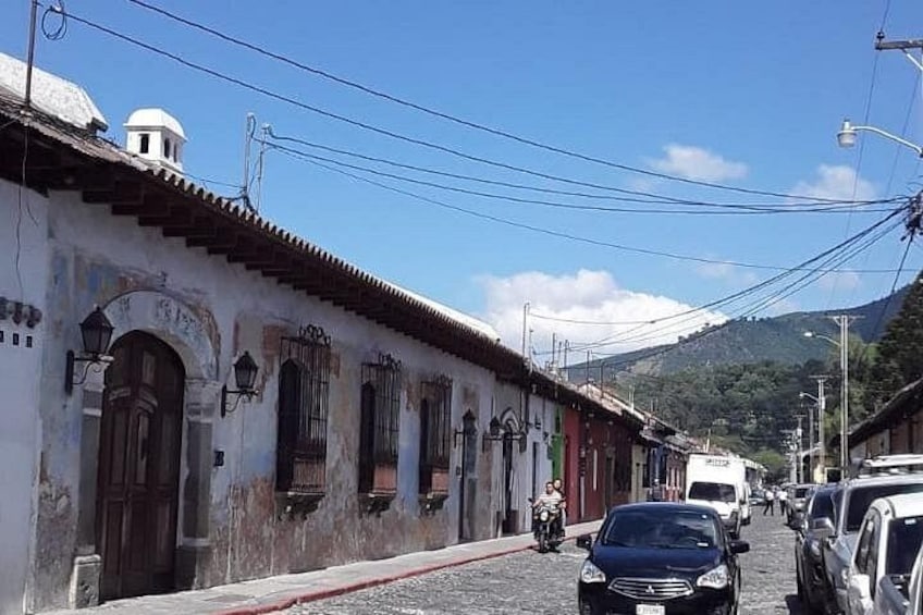 A cobblestone street lined with historic buildings, a motorbike, and parked cars. 2