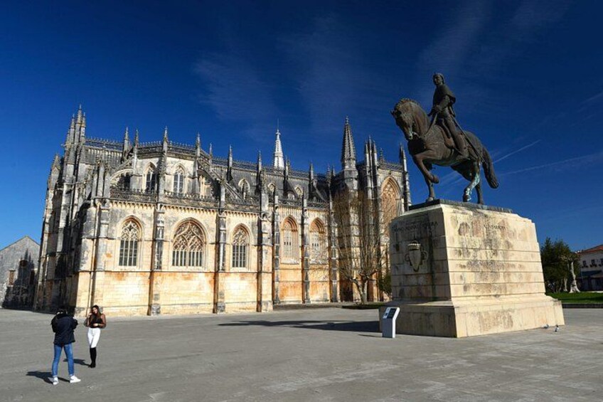 A cathedral with Gothic architecture, a statue of a historical figure on horseback, and a clear blue sky. 1