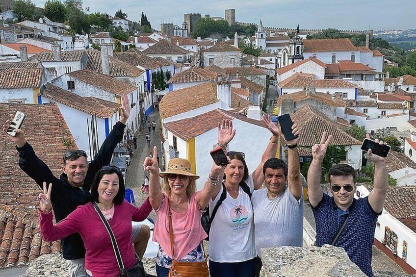 A group of people standing on a high vantage point overlooking a town with terracotta-roofed buildings. 4